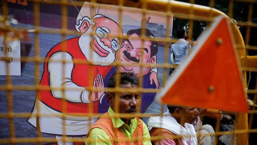 FILE PHOTO: A man sits next to a poster put up during a protest by India's main opposition Congress party against Indian billionaire Gautam Adani, in New Delhi