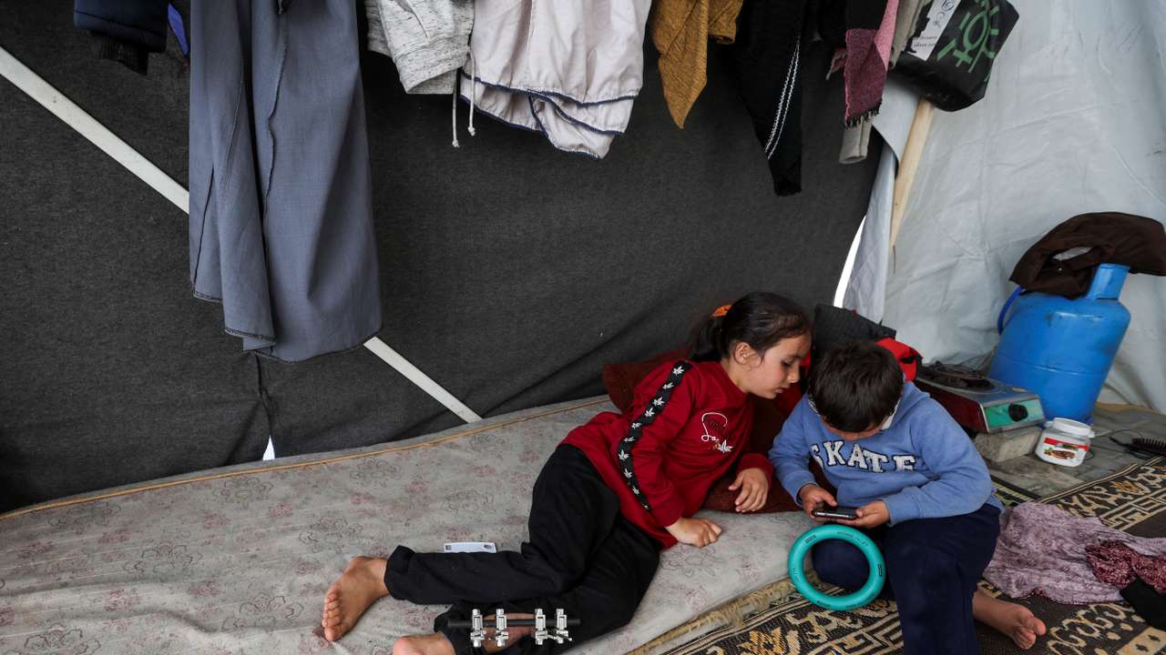 Laila Al-Sultant, a displaced Palestinian girl who was wounded in an Israeli strike that killed her father, plays with her brother Khaled inside their makeshift shelter, in Rafah in the southern Gaza Strip