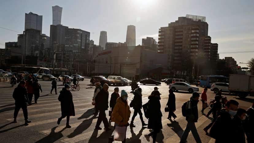 People cross a street during morning rush hour in front of the skyline of the CBD in Beijing