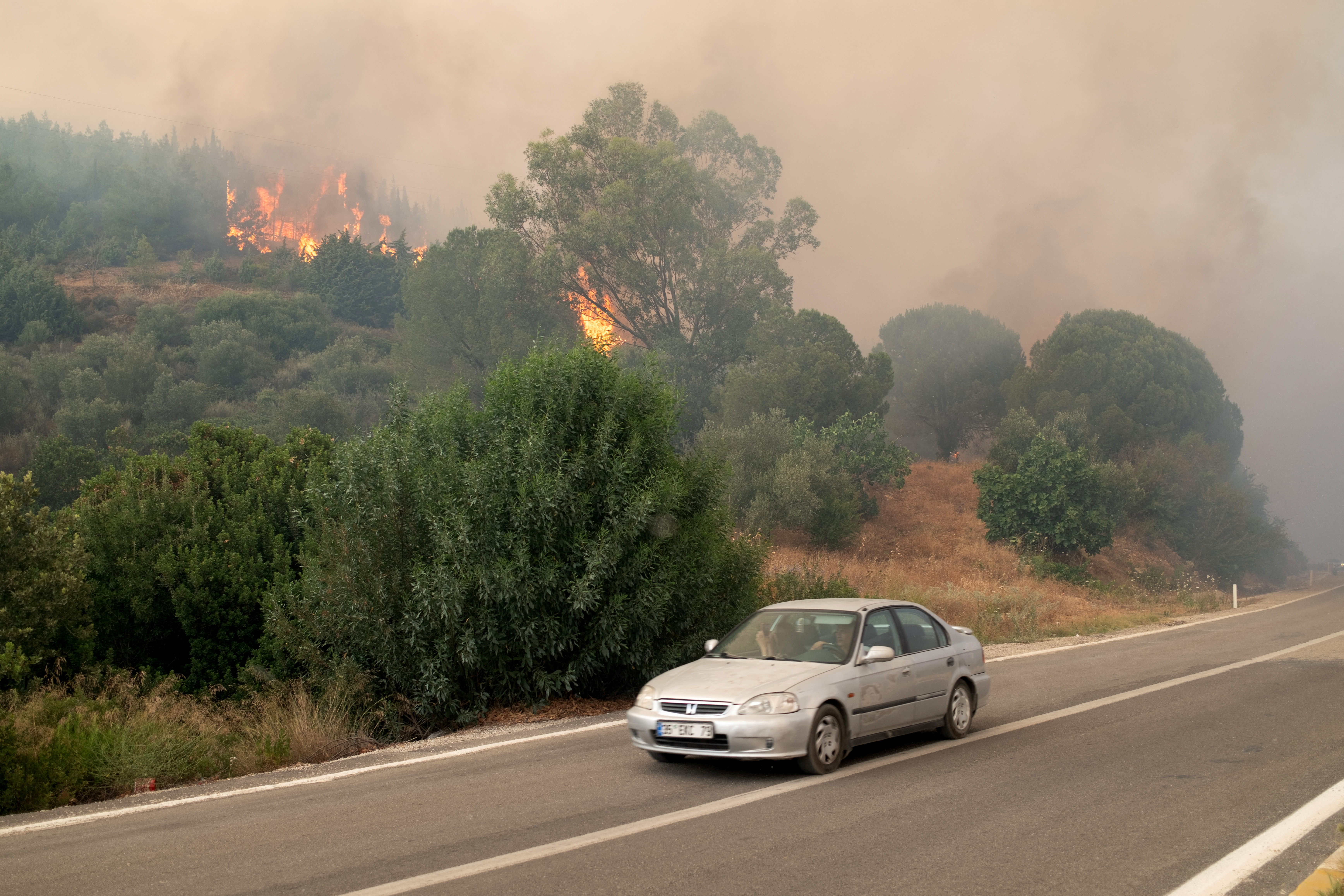 A car drives past as a wildfire burns near Seferihisar in Izmir province