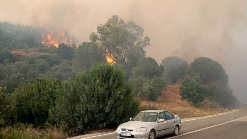 A car drives past as a wildfire burns near Seferihisar in Izmir province