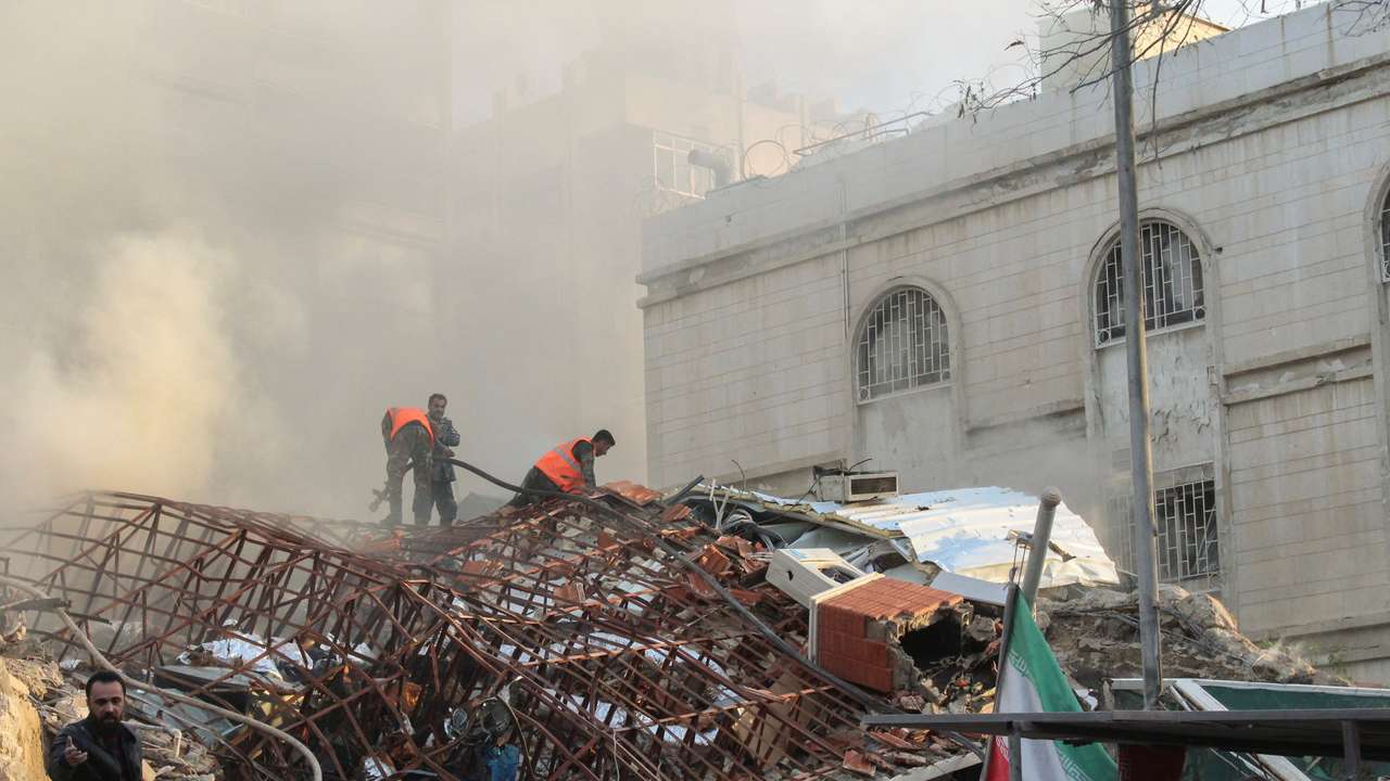Members of the civil defence stand near a damaged site after what Syrian and Iranian media described as an Israeli air strike on Iran's consulate in the Syrian capital Damascus