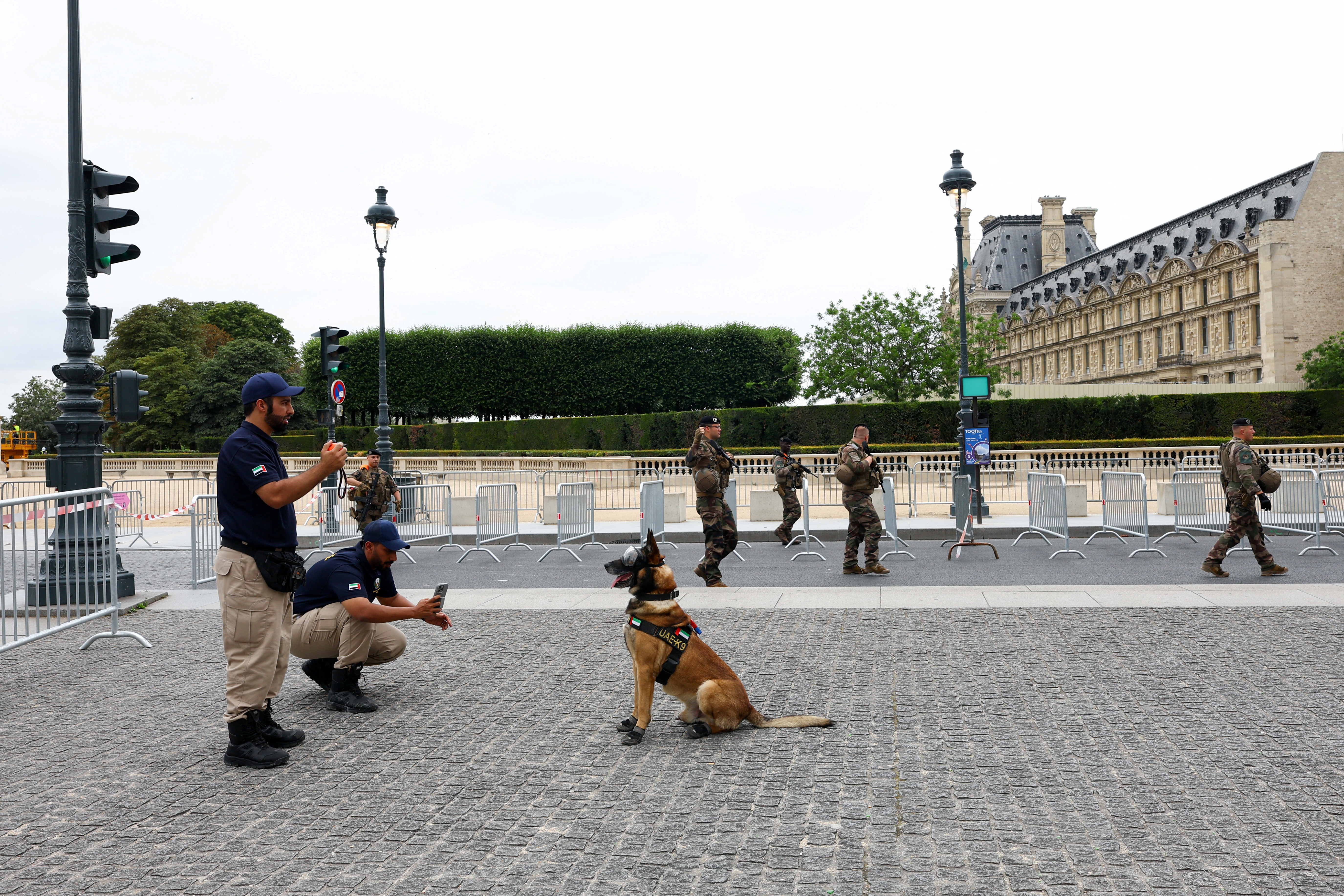 Law enforcement officer photographs dog as members of special task force walk past, at Louvre in Paris