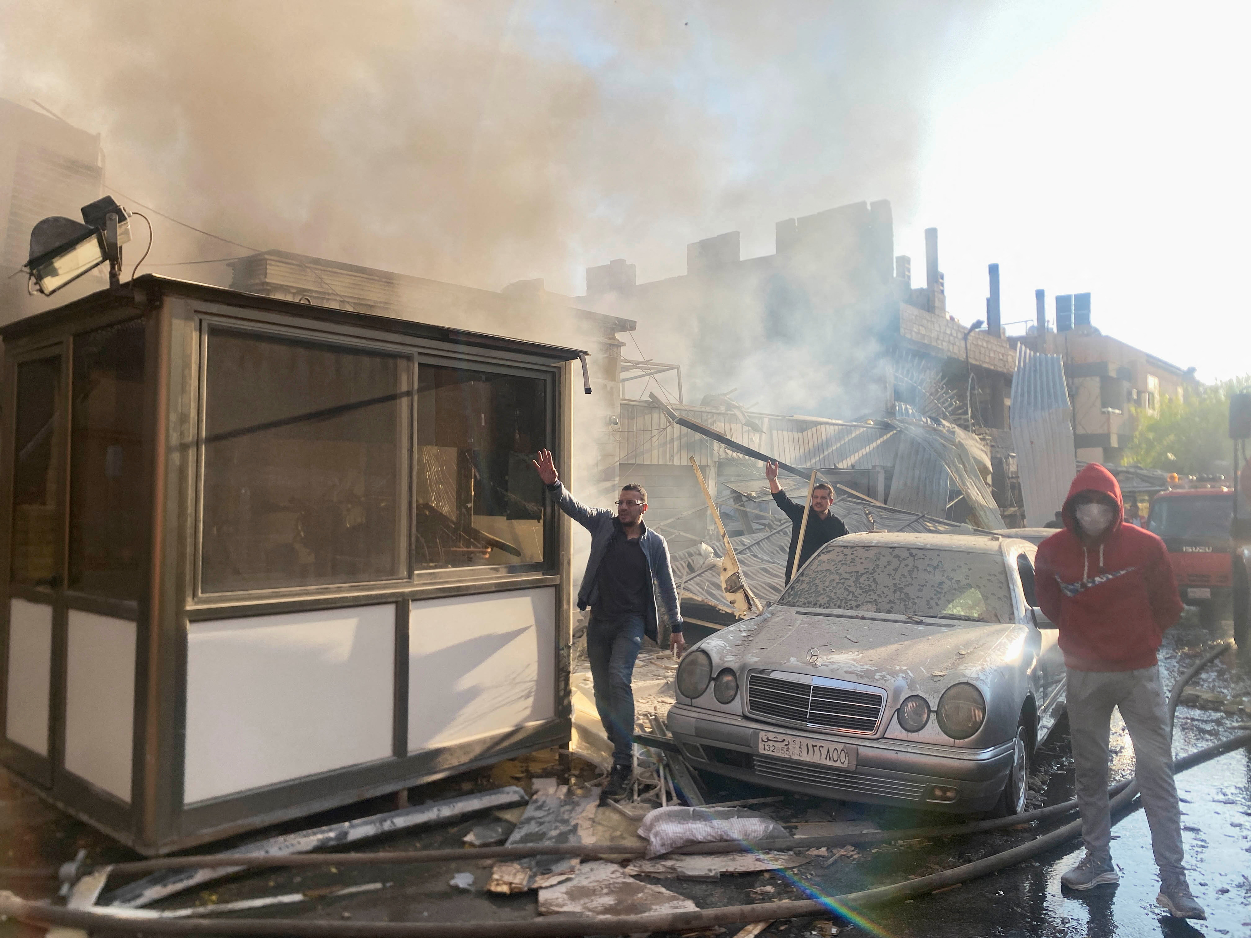 Smoke rises as people gesture at a damaged site after what Syrian state news agency said was an Israeli strike in Damascus suburb of Mazzeh