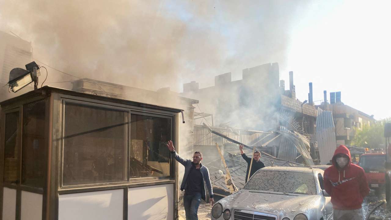 Smoke rises as people gesture at a damaged site after what Syrian state news agency said was an Israeli strike in Damascus suburb of Mazzeh