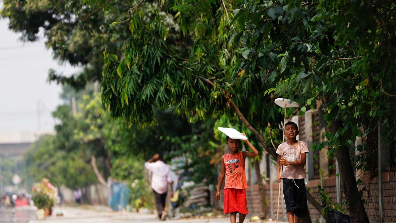 Children hold cork sheets to cover them from the sun while walking along a street during a countrywide heatwave in Dhaka