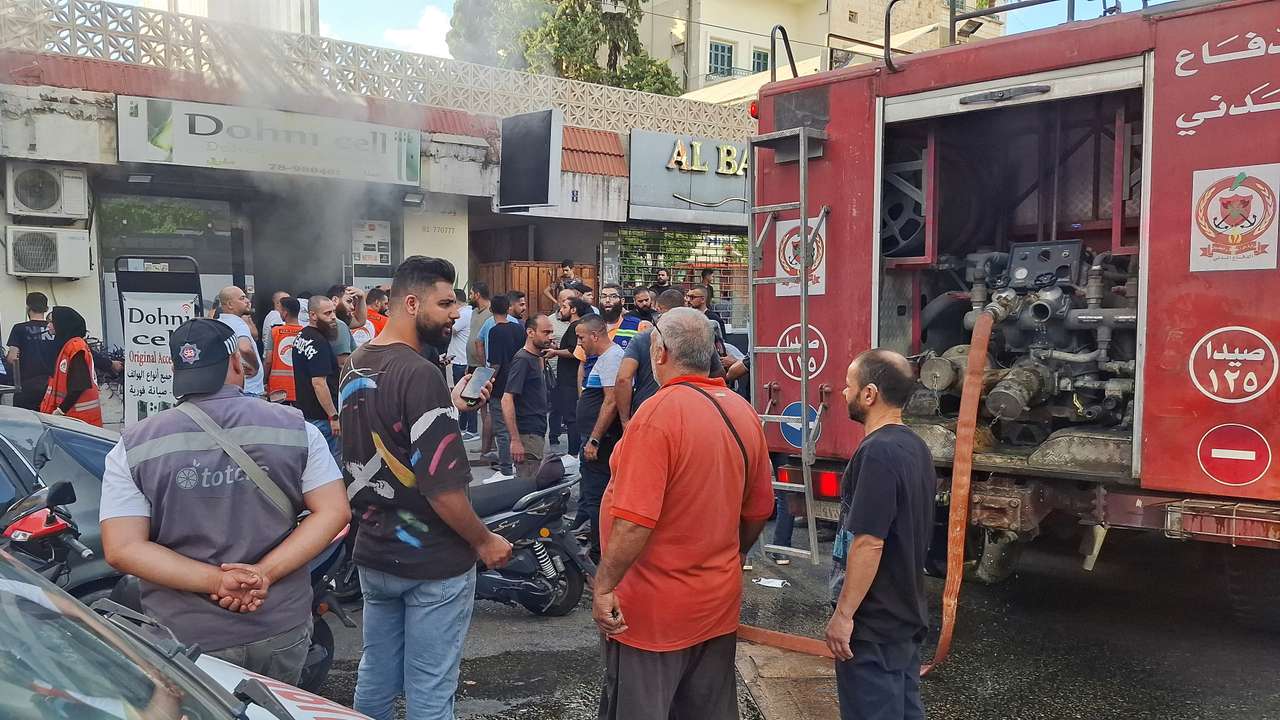 People gather as smoke rises from a mobile shop in Sidon