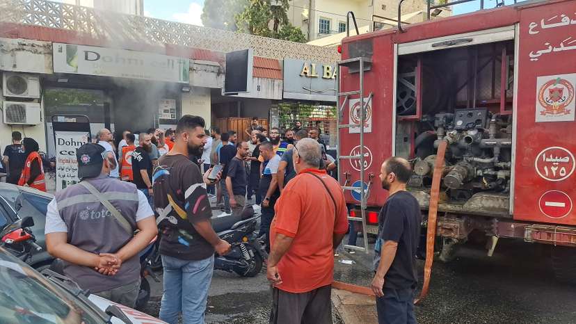 People gather as smoke rises from a mobile shop in Sidon