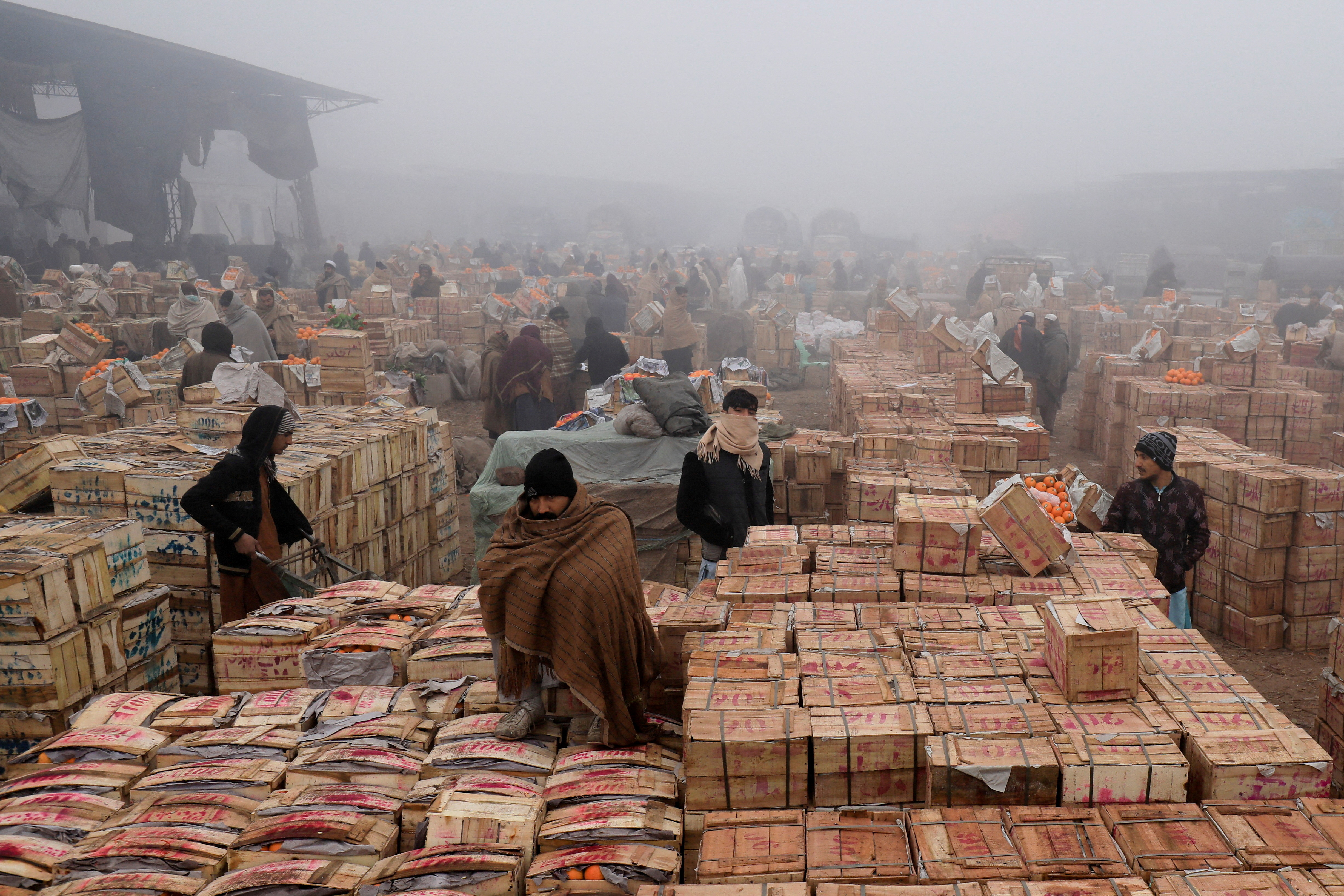 FILE PHOTO: People cover themselves to stay warm during heavy fog, early in the morning at the fruit wholesale market on the outskirts of Peshawarr