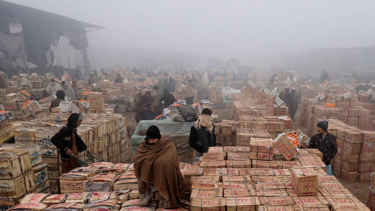 FILE PHOTO: People cover themselves to stay warm during heavy fog, early in the morning at the fruit wholesale market on the outskirts of Peshawarr