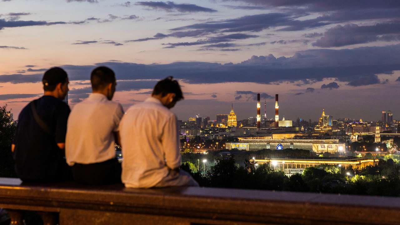 People sit on the parapet at Vorobyovy Gory viewpoint with the city’s skyline seen in the background in Moscow