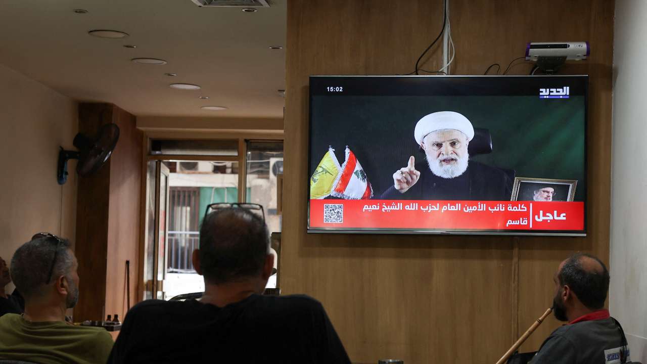 People watch Hezbollah deputy leader Sheikh Naim Qassem delivering a televised address, as they sit in a cafe in Beirut