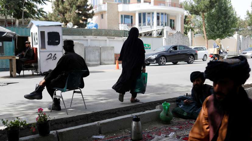 An Afghan woman walks among Taliban soldiers at a checkpoint in Kabul