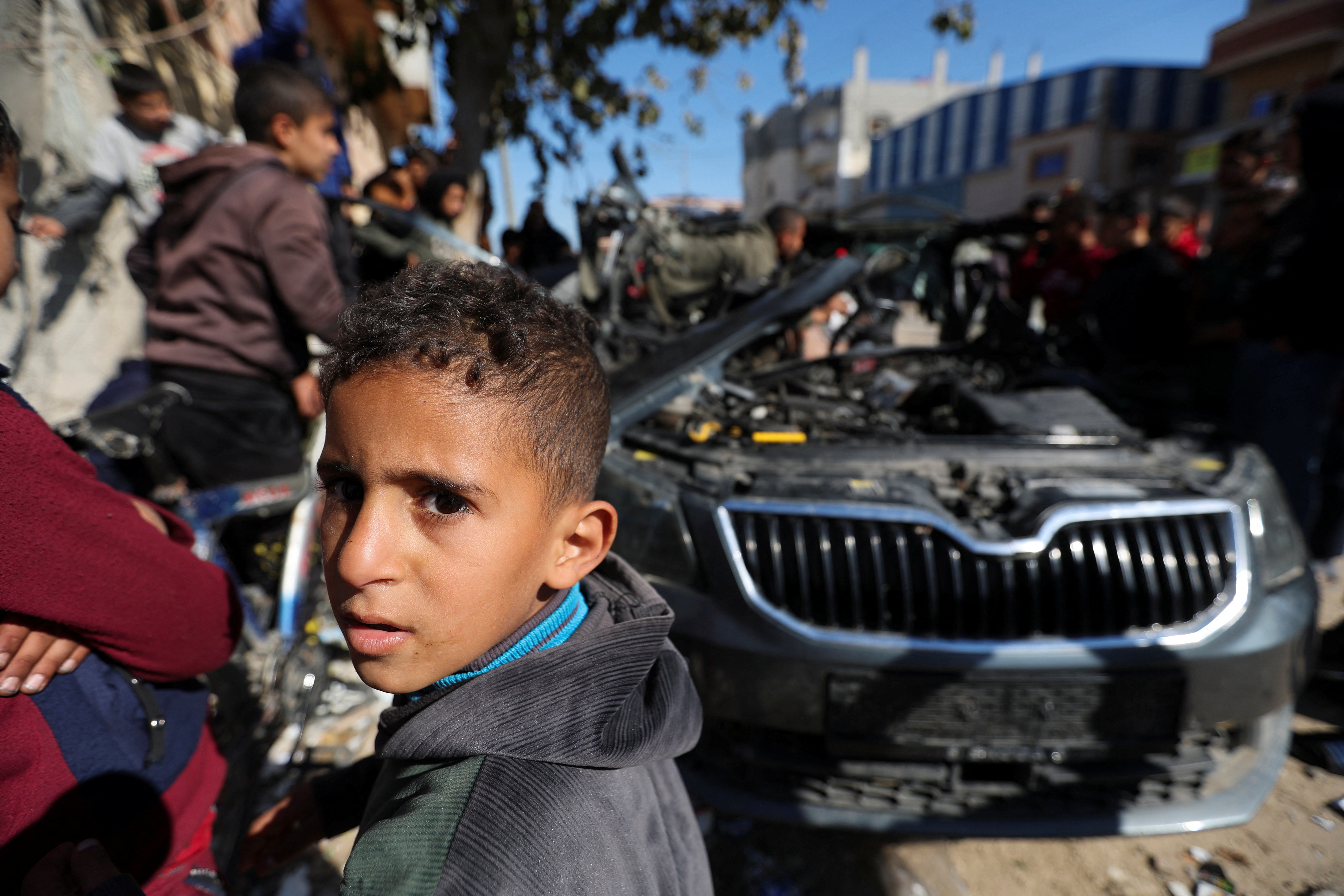 Palestinians inspect the remains of a car where Palestinian journalist Hamza Al-Dahdouh was killed along with another journalist in an Israeli strike, in Rafah