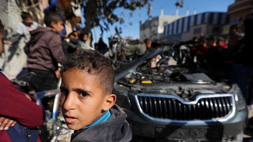 Palestinians inspect the remains of a car where Palestinian journalist Hamza Al-Dahdouh was killed along with another journalist in an Israeli strike, in Rafah