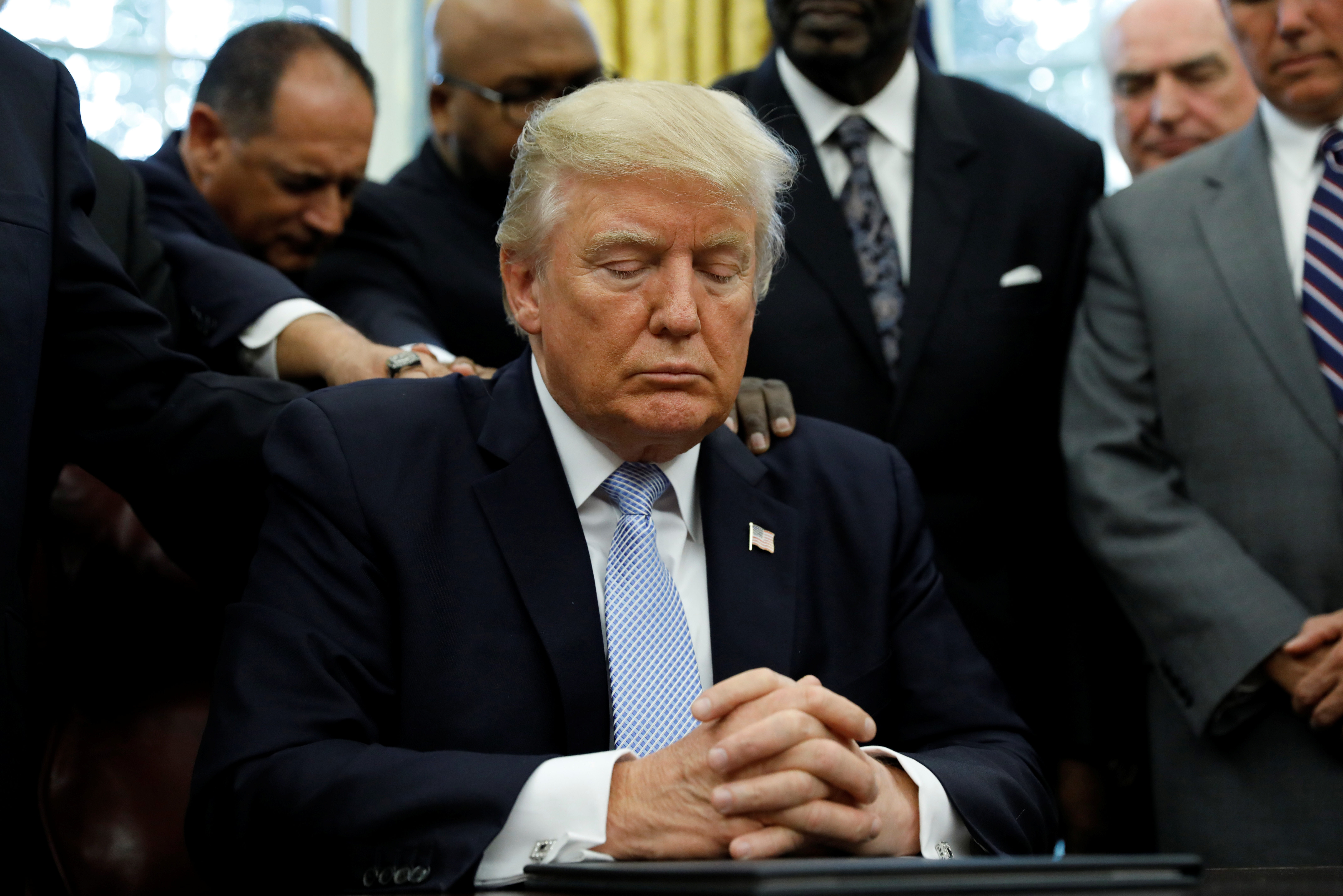 Faith leaders place their hands on the shoulders of U.S. President Trump as he takes part in a prayer for those affected by Hurricane Harvey in the Oval Office of the White House in Washington
