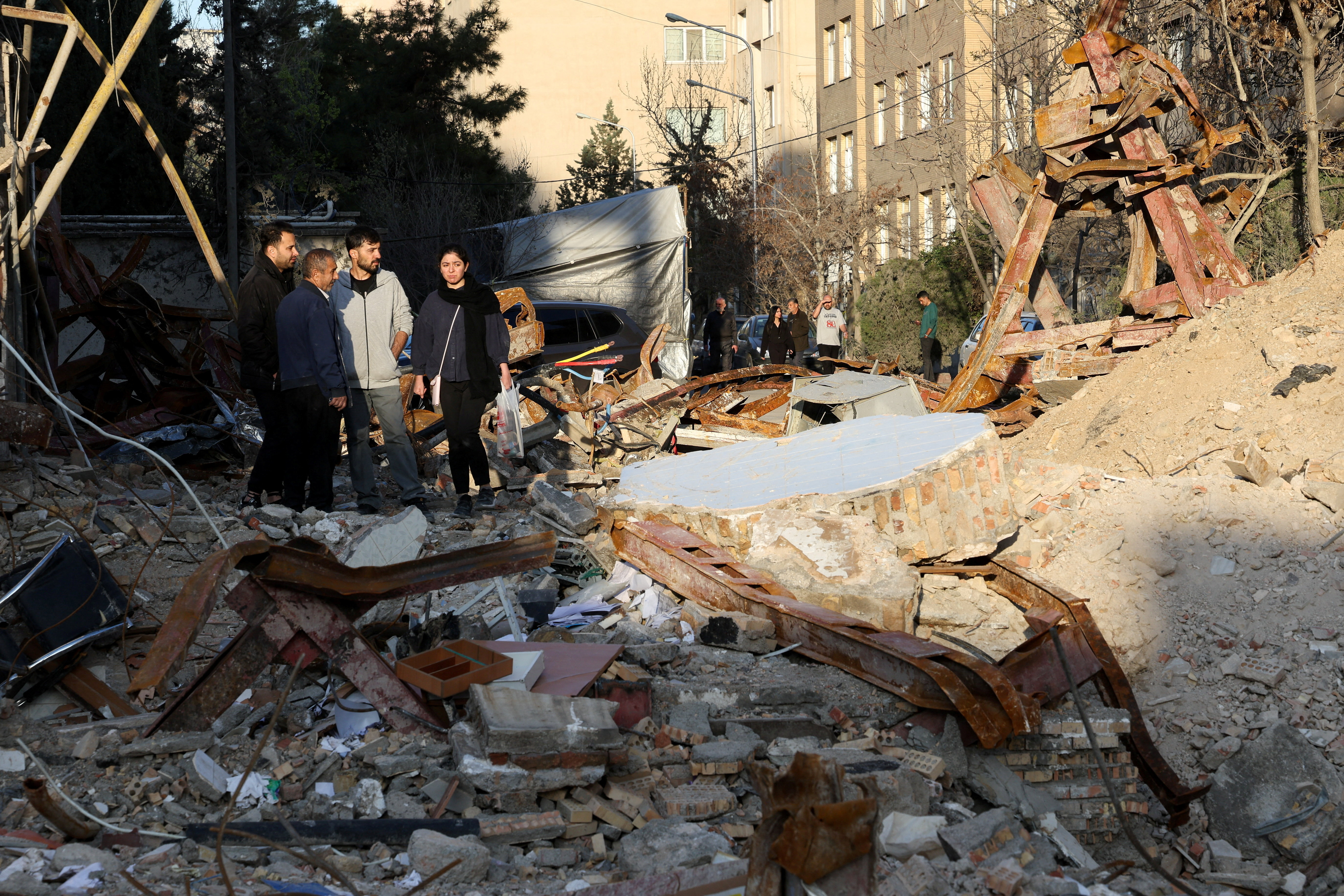 People look at a destroyed building following a strike, in Tehran