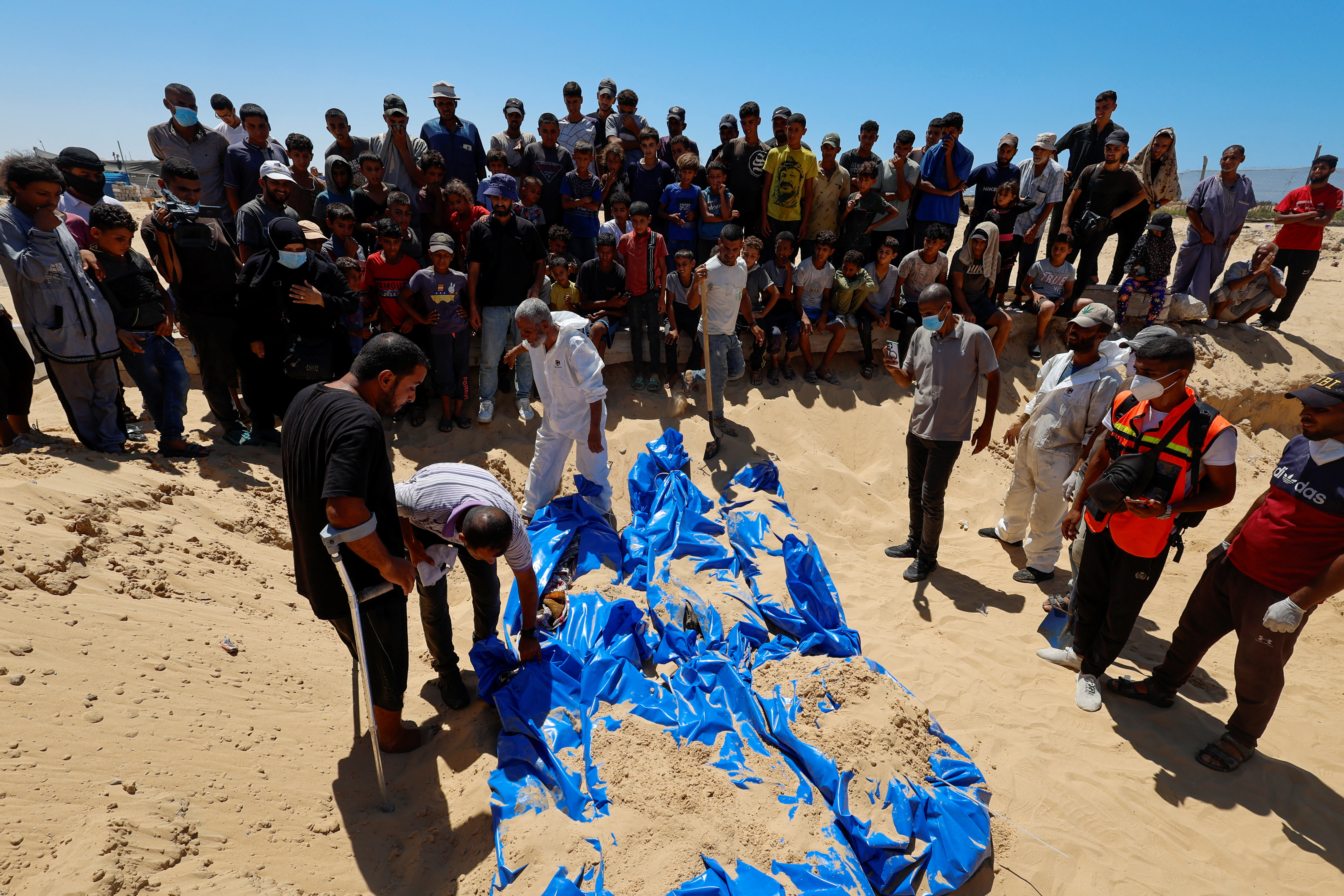 People bury the bodies of unidentified Palestinians at a mass grave after the bodies were handed over by Israel, in Khan Younis