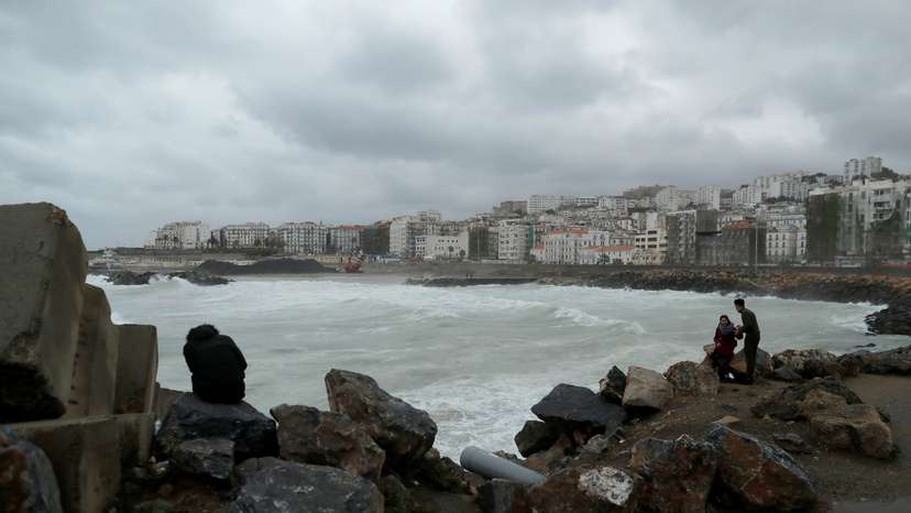 People are pictured in the rainy day on the edge of the Ketani beach at Bab El Oued in Algiers