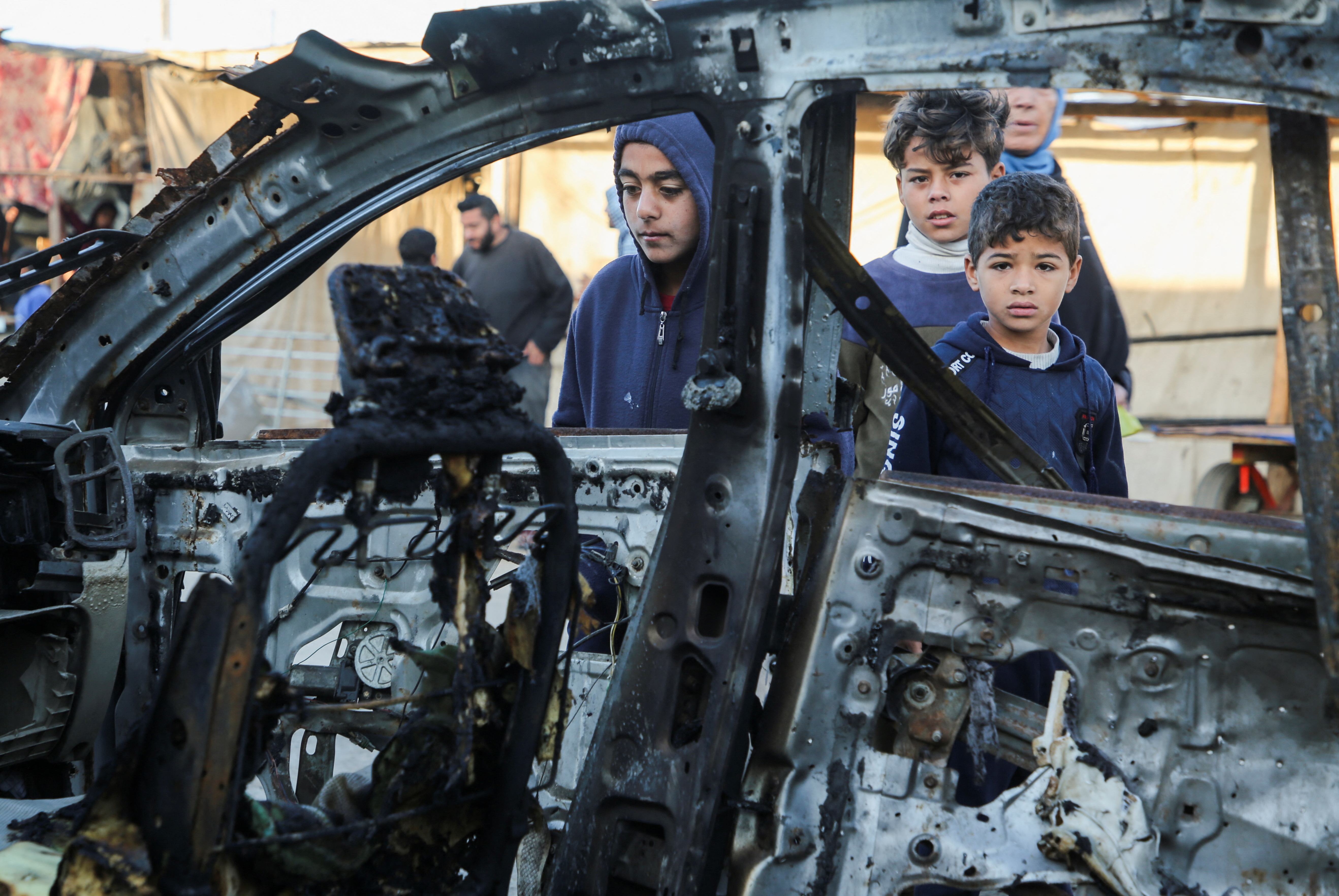 Palestinians inspect the remains of a car in the aftermath of an Israeli strike, in Khan Younis