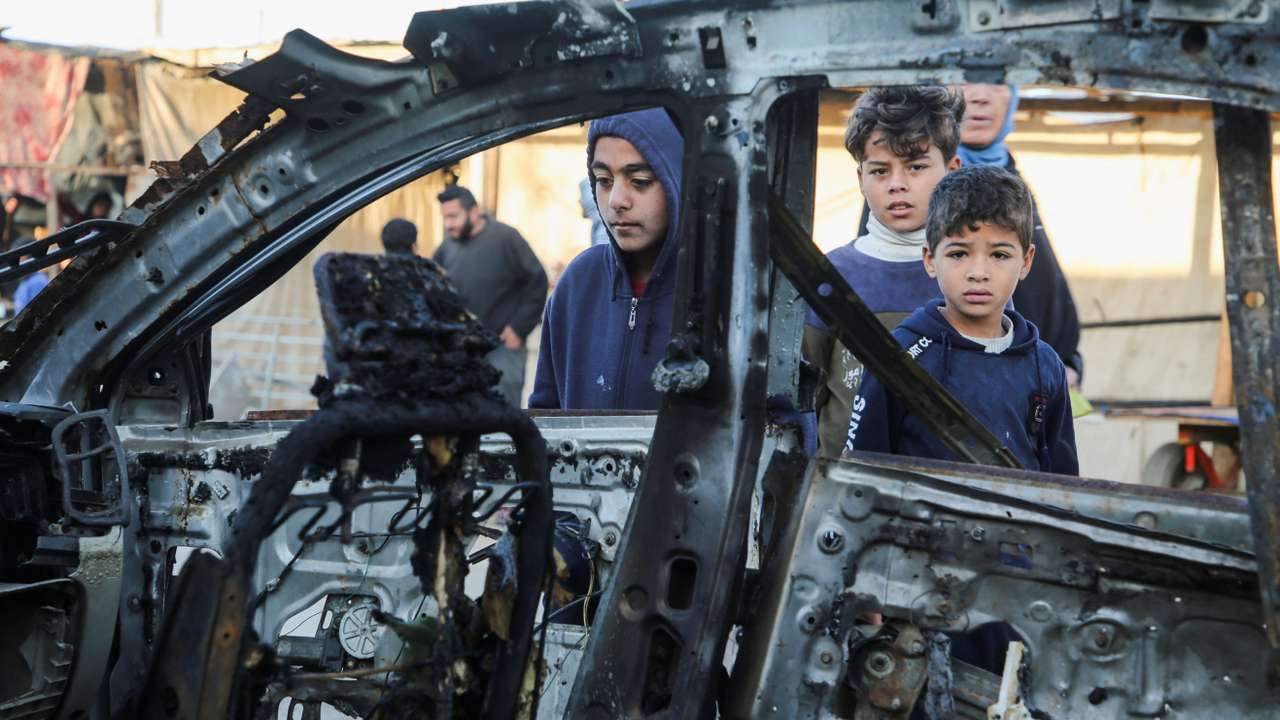 Palestinians inspect the remains of a car in the aftermath of an Israeli strike, in Khan Younis