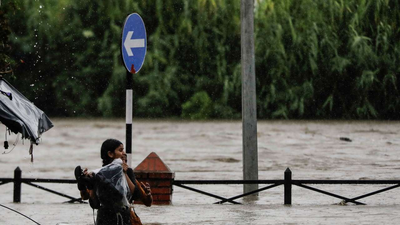 A woman carrying her belongings wades through a flooded road along the bank of overflowing Bagmati River following heavy rains in Kathmandu