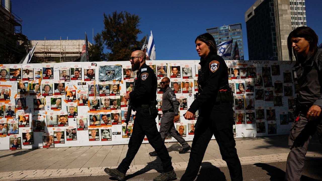 Israeli police officers walk past a board displaying pictures of hostages kidnapped in the deadly October 7 attack, in Tel Aviv