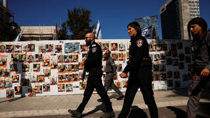 Israeli police officers walk past a board displaying pictures of hostages kidnapped in the deadly October 7 attack, in Tel Aviv