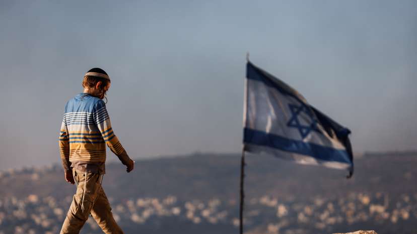 A Jewish settler teenager walks by an Israeli flag in Givat Eviatar, a new Israeli settler outpost, near the Palestinian village of Beita in the Israeli-occupied West Bank
