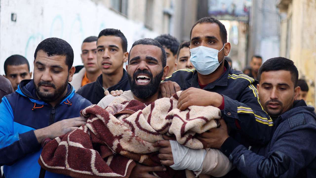 A Palestinian man carries a child casualty at the site of Israeli strikes on houses, in Rafah