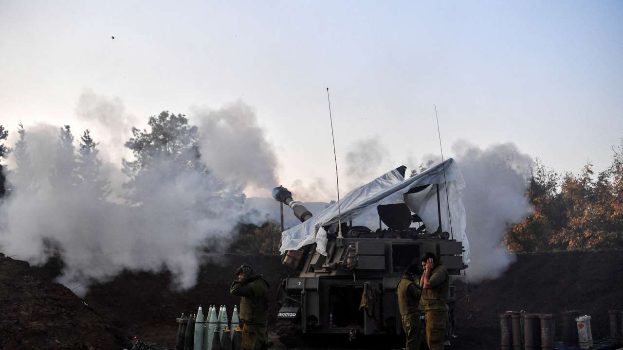 Israeli soldiers stand by, as a mobile artillery unit fires, on the Israeli side of the Israel-Lebanon border