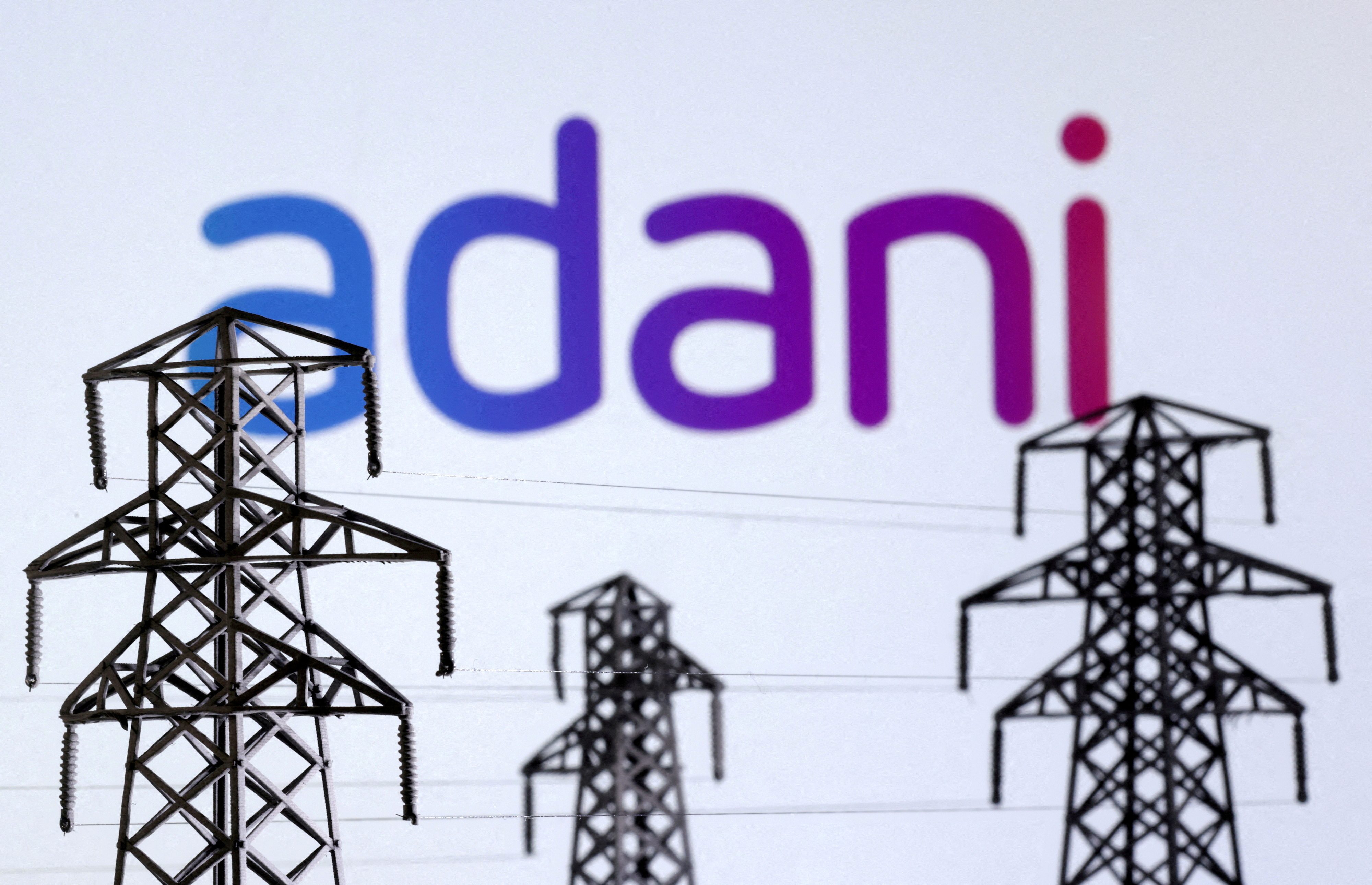FILE PHOTO: Illustration shows Electric power transmission pylon miniatures and Adani Green Energy logo