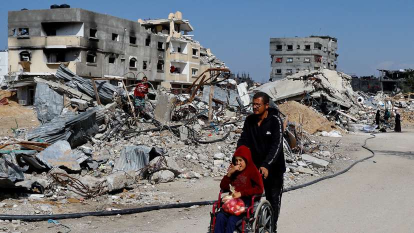 A Palestinian man pushes a child on a wheelchair amidst the rubble of buildings destroyed during the Israeli offensive, amid a ceasefire between Israel and Hamas, in Rafah