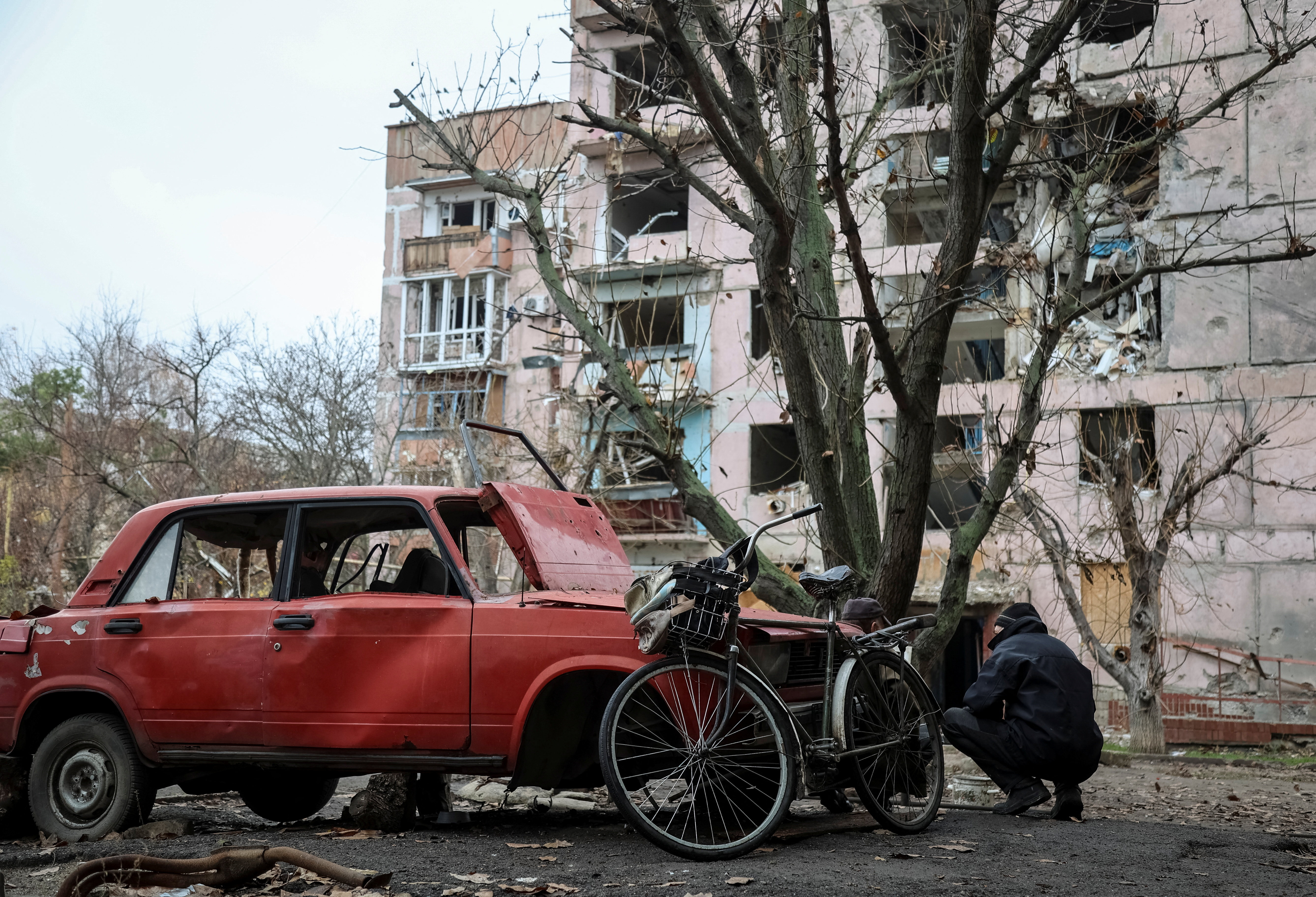 A resident hides from a Russian FPV drone behind a damaged car in the frontline town of Huliaipole