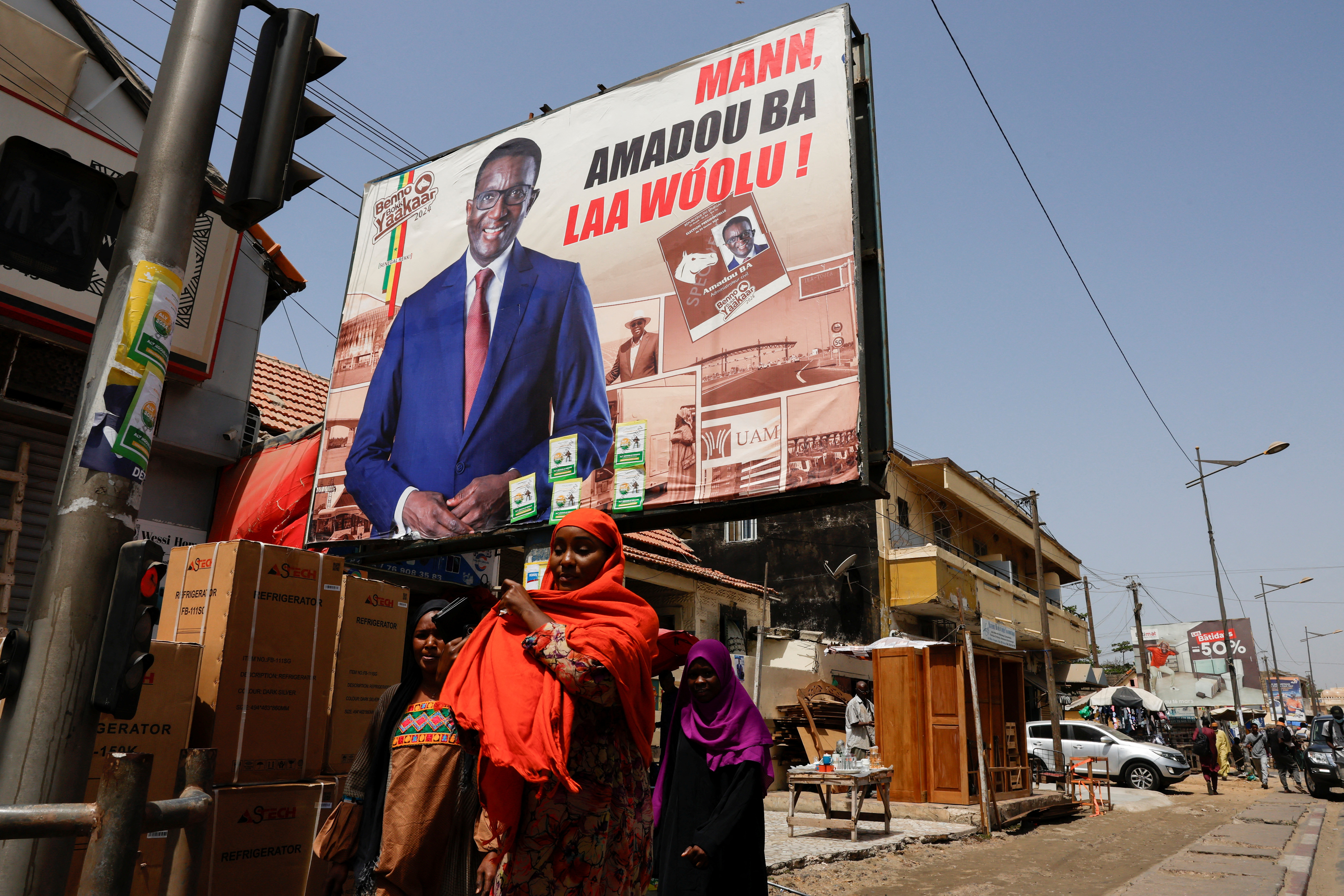People walk past an electoral billboard of the Senegalese presidential candidate, Amadou Ba of Senegalese President Macky Sall's ruling coalition in a street in Dakar