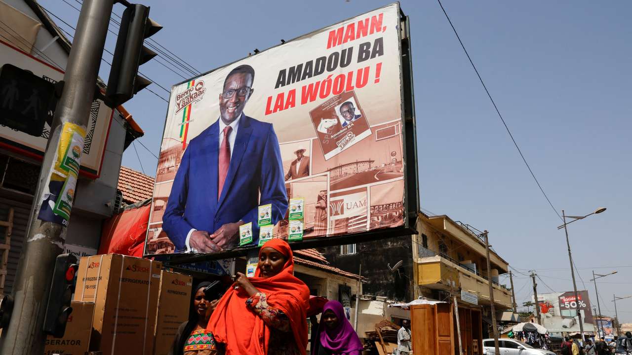 People walk past an electoral billboard of the Senegalese presidential candidate, Amadou Ba of Senegalese President Macky Sall's ruling coalition in a street in Dakar