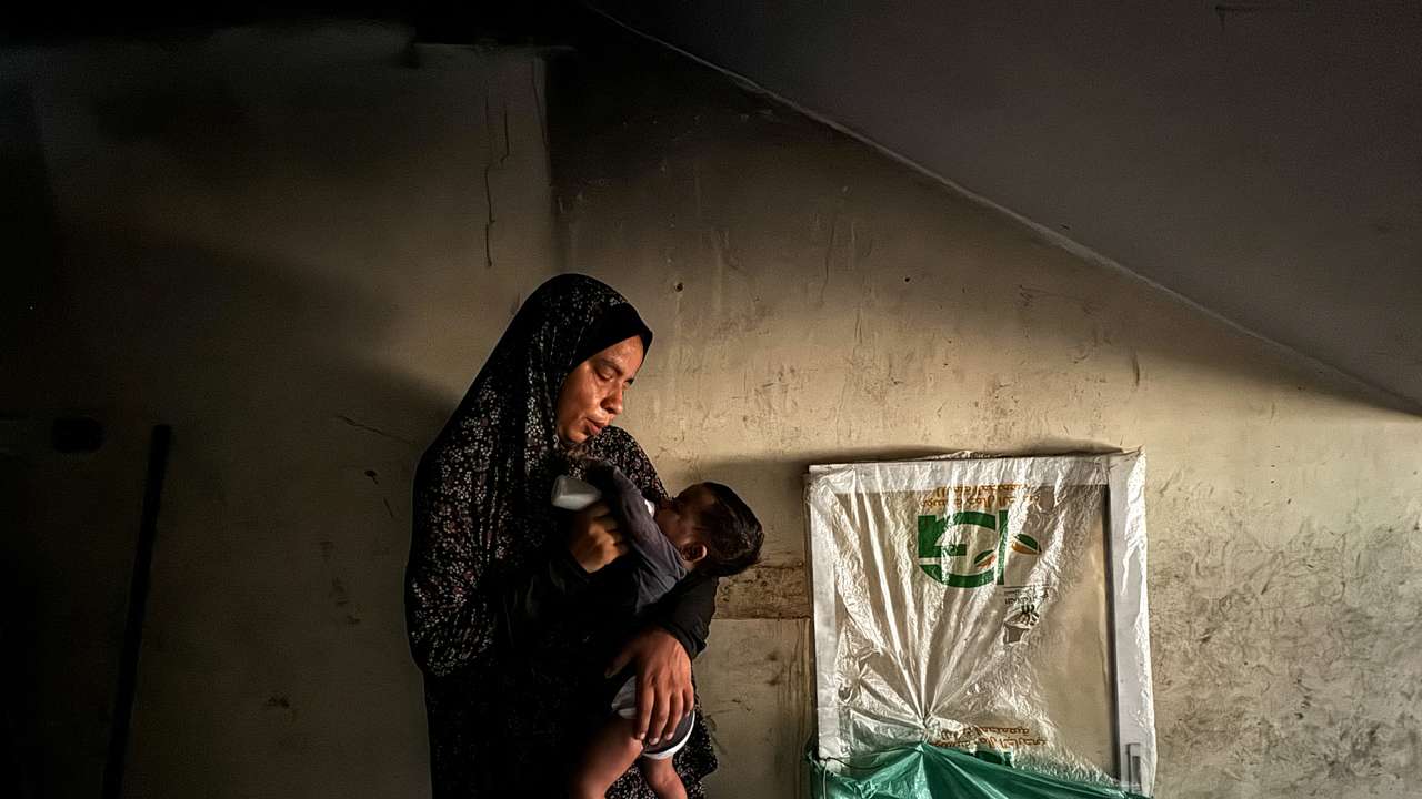 A displaced Palestinian woman helps her son drinks milk at a school classroom where she shelters, amid food scarcity, as Israel-Hamas conflict continues, in Khan Younis