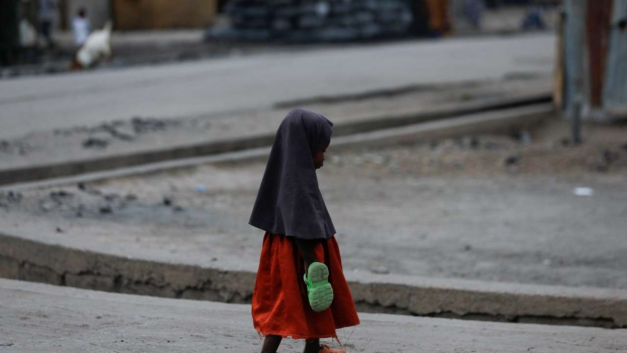 A girl carrying an extra pair of slippers, walks along the road in Maiduguri