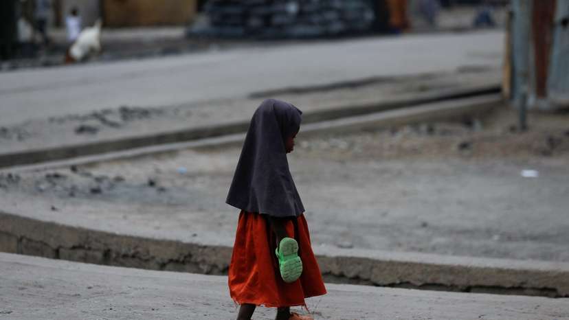 A girl carrying an extra pair of slippers, walks along the road in Maiduguri