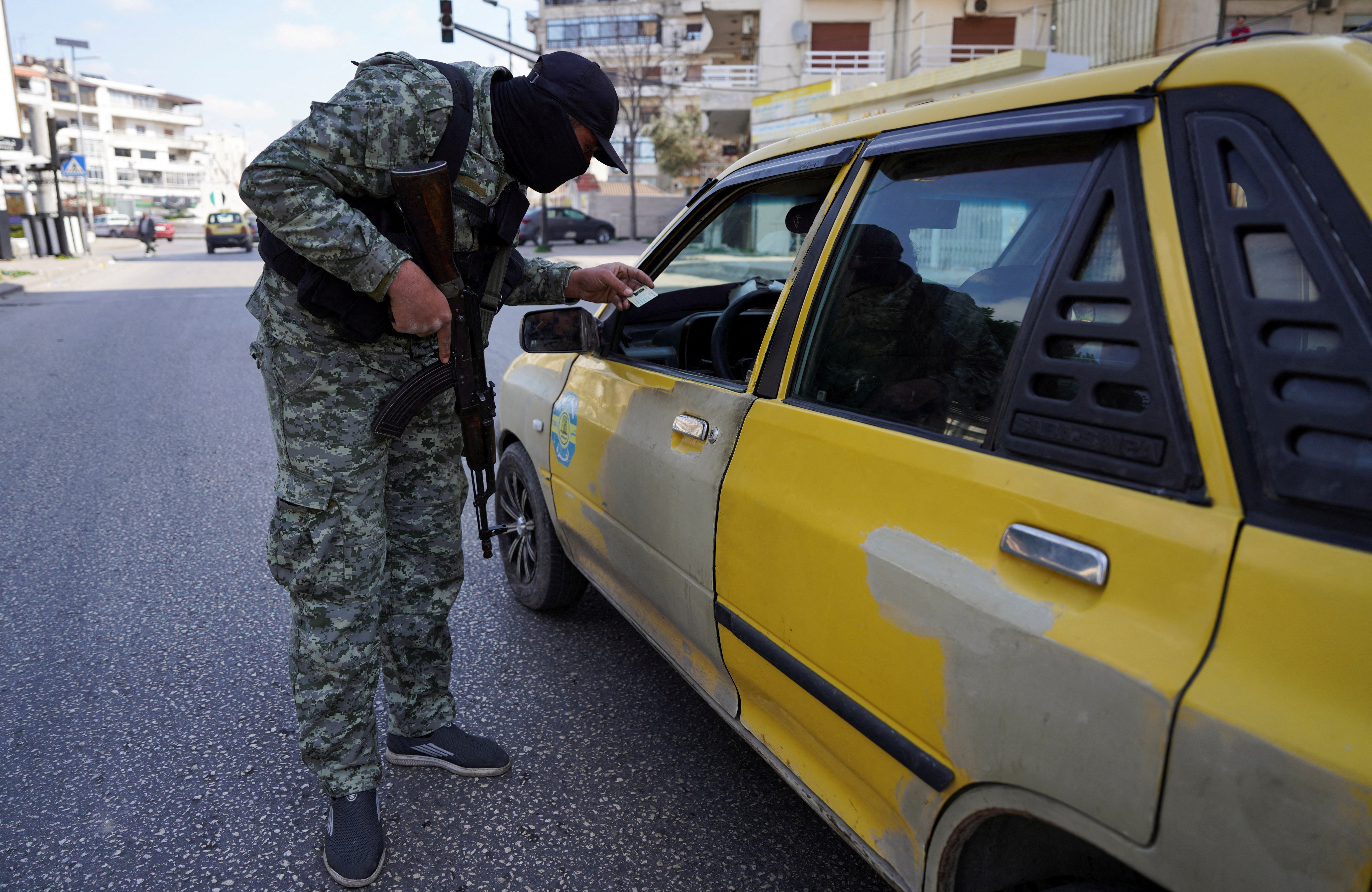 FILE PHOTO: A member of the Syrian security forces checks an ID of a person, in Latakia