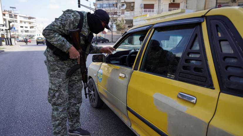 FILE PHOTO: A member of the Syrian security forces checks an ID of a person, in Latakia