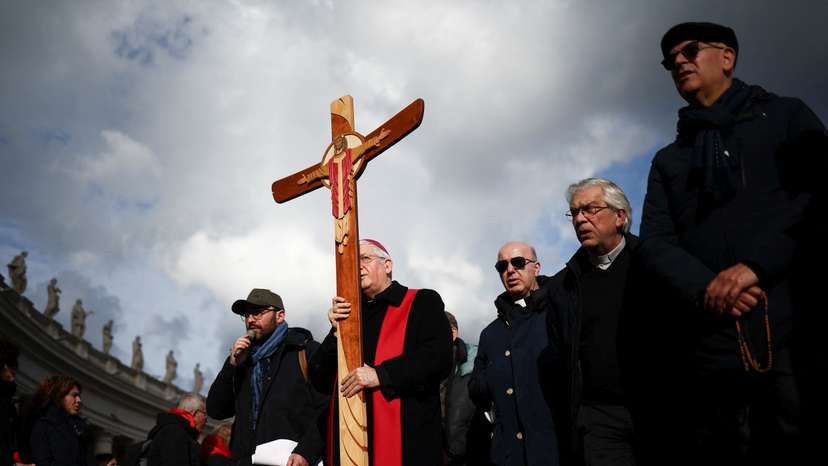 A bishop carries a cross at St. Peter's Square at the Vatican, as Pope Francis continues his hospitalization