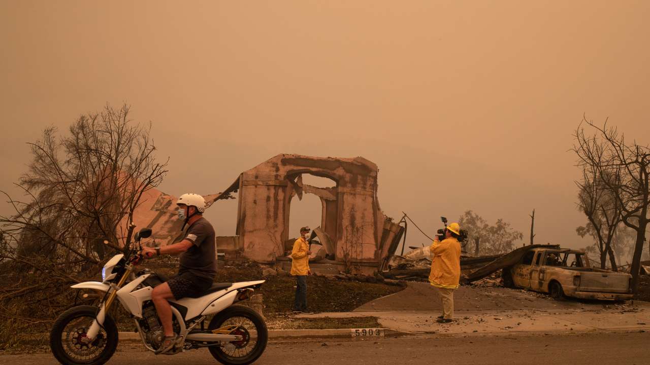 FILE PHOTO: A man rides past journalists reporting on the aftermath of the Shady Fire after it advanced into the Skyhawk neighborhood of Santa Rosa