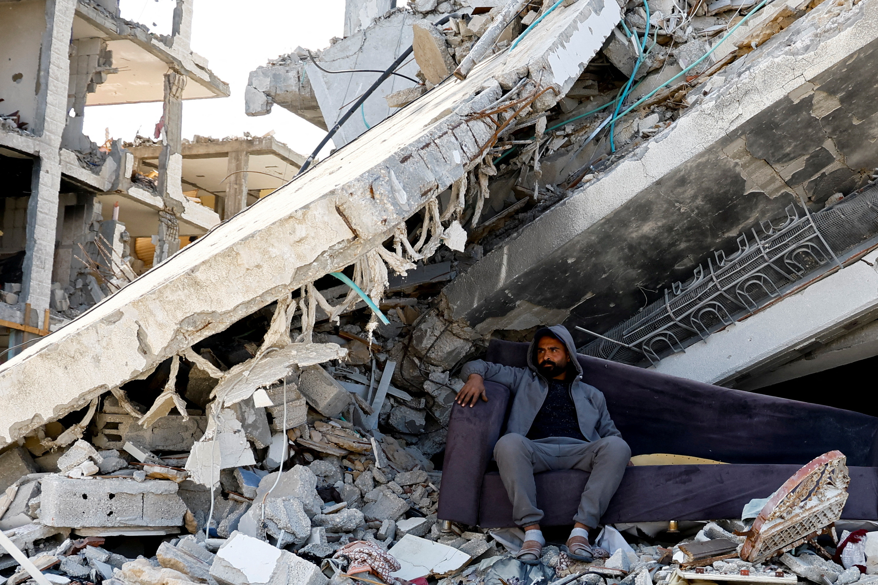 A Palestinian man sits amidst the rubble of buildings destroyed during the Israeli offensive, amid a ceasefire between Israel and Hamas, in Rafah