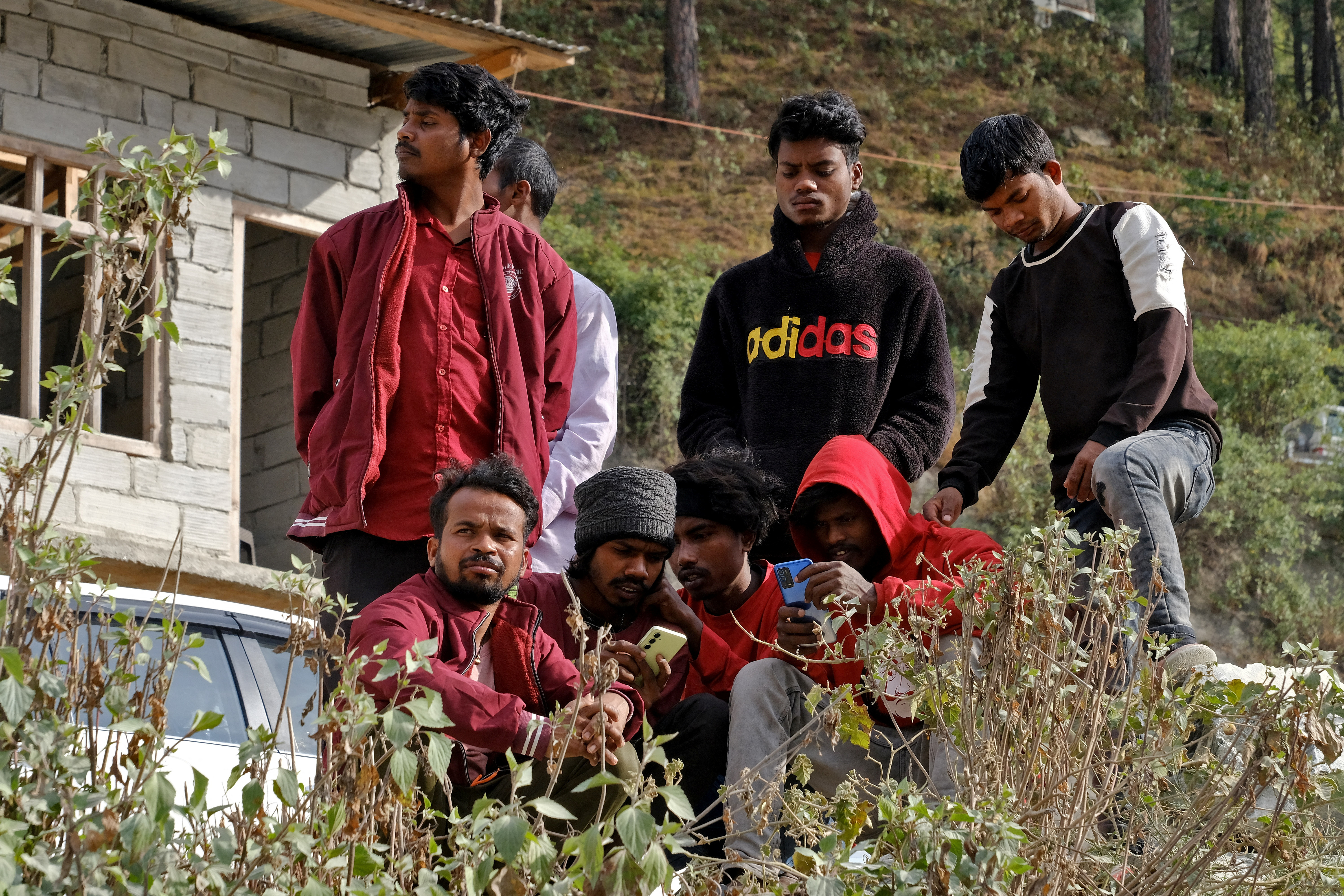 Relatives of the trapped workers watch their mobile phones as they wait outside the collapsed tunnel in Uttarkashi