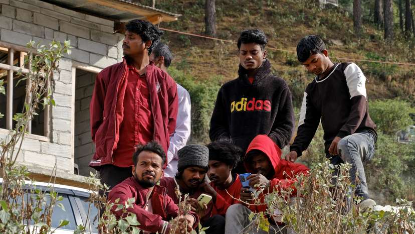 Relatives of the trapped workers watch their mobile phones as they wait outside the collapsed tunnel in Uttarkashi