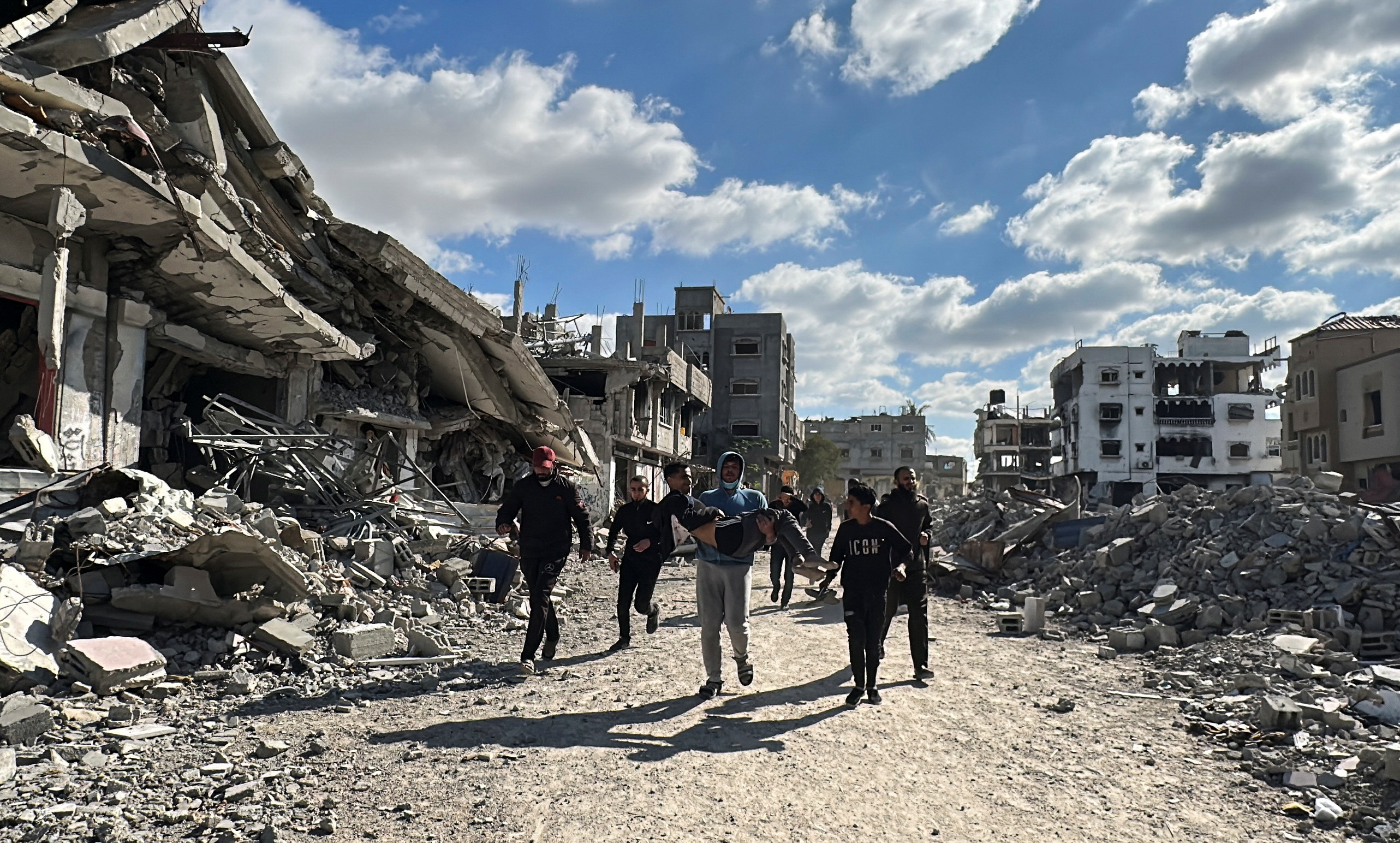 Palestinians walk past the rubble of houses and buildings destroyed during the war, in Al-Bureij