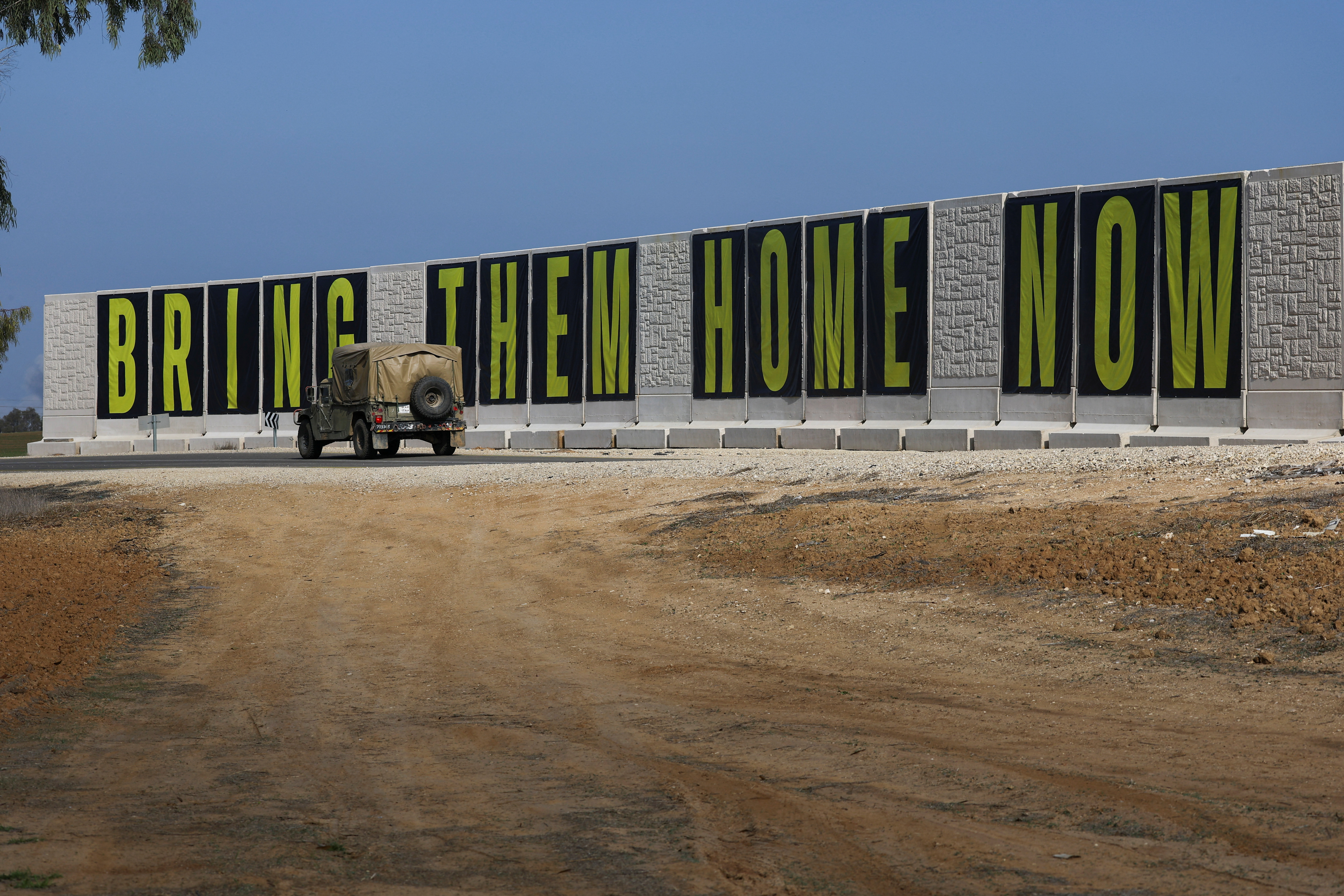 An Israeli Military vehicle drives past banners reading " Bring Them Home Now" near the Israel-Gaza border