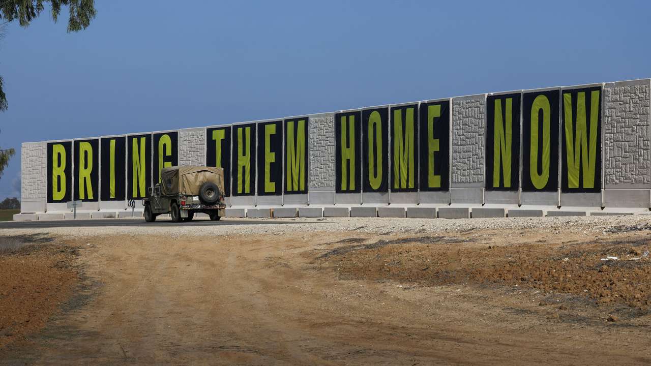 An Israeli Military vehicle drives past banners reading " Bring Them Home Now" near the Israel-Gaza border