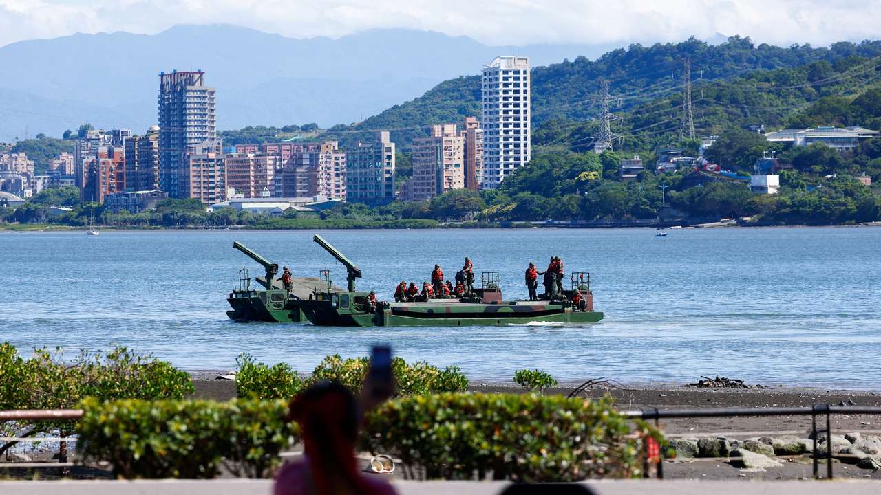 A woman watches as soldiers practice laying mines and nets to stymie the landing of enemy forces at the mouth of a major river in Taipei